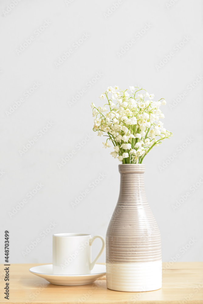 浅墙上的桌子上放着铃兰花和一杯咖啡的花瓶