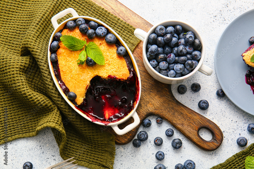 Composition with blueberry cobbler in baking dish on light background