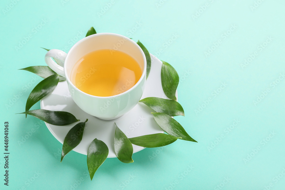Cup of tea and green leaves on color background, closeup
