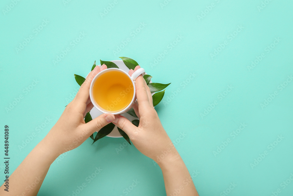Female hands with cup of tea and green leaves on color background