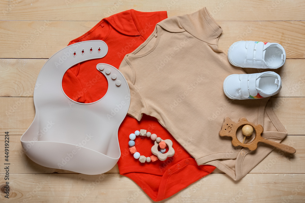 木制背景的婴儿衣服、鞋子、围兜和玩具