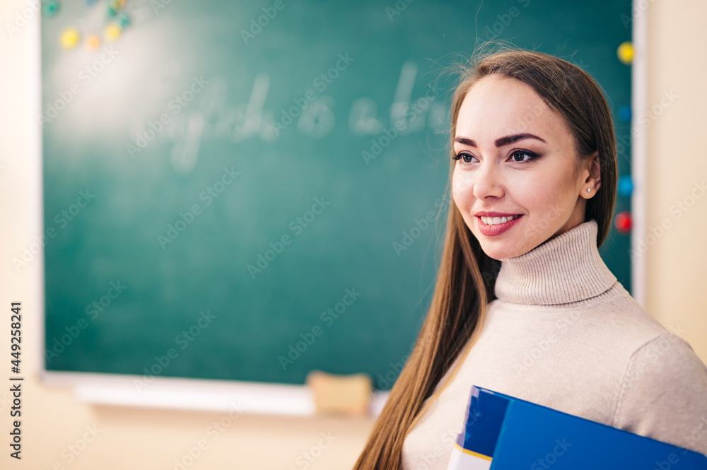 教室里年轻漂亮的老师。老师在学校或大学的教室里拿着文件夹。E