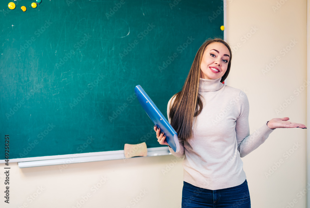 学生女孩站在教室干净的黑板旁，手里拿着打开的笔记。学校和教育部