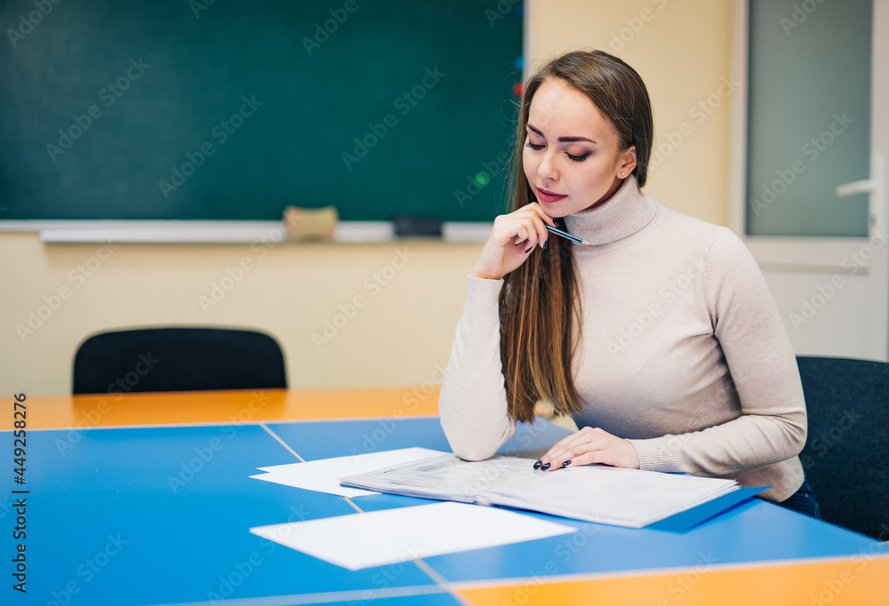 漂亮的年轻老师，课间休息时坐在桌子旁看笔记。女老师