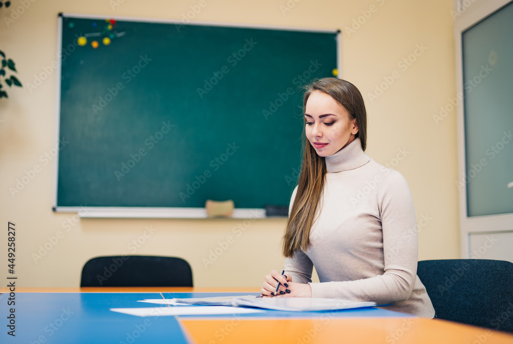 漂亮的年轻老师坐在桌子旁检查笔记。教室里的女老师。黑人