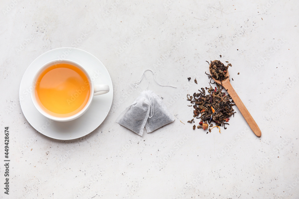 Cup with tasty tea, dry leaves and bags on light background