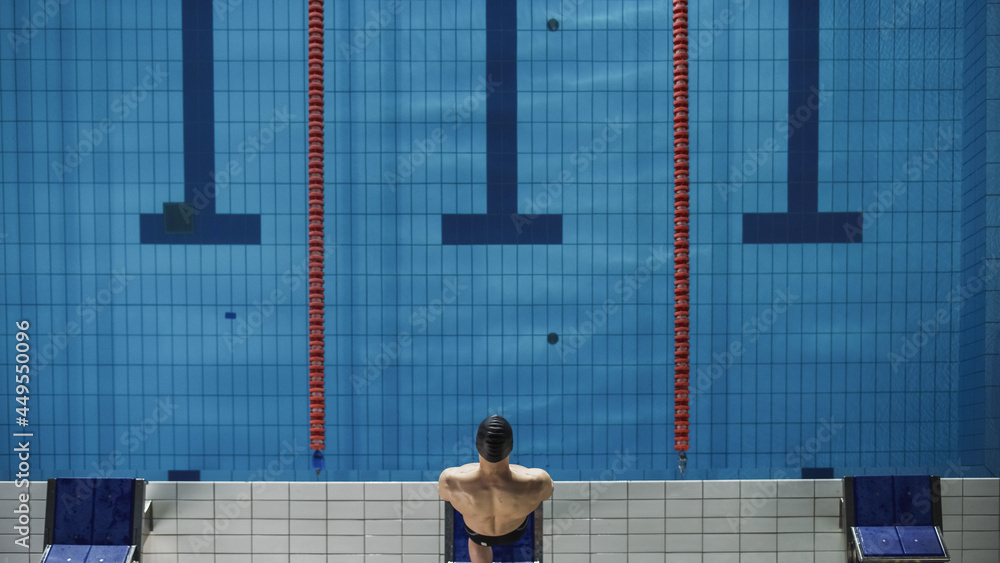空中俯视图男游泳运动员站在起跑台上，准备跳入游泳池。