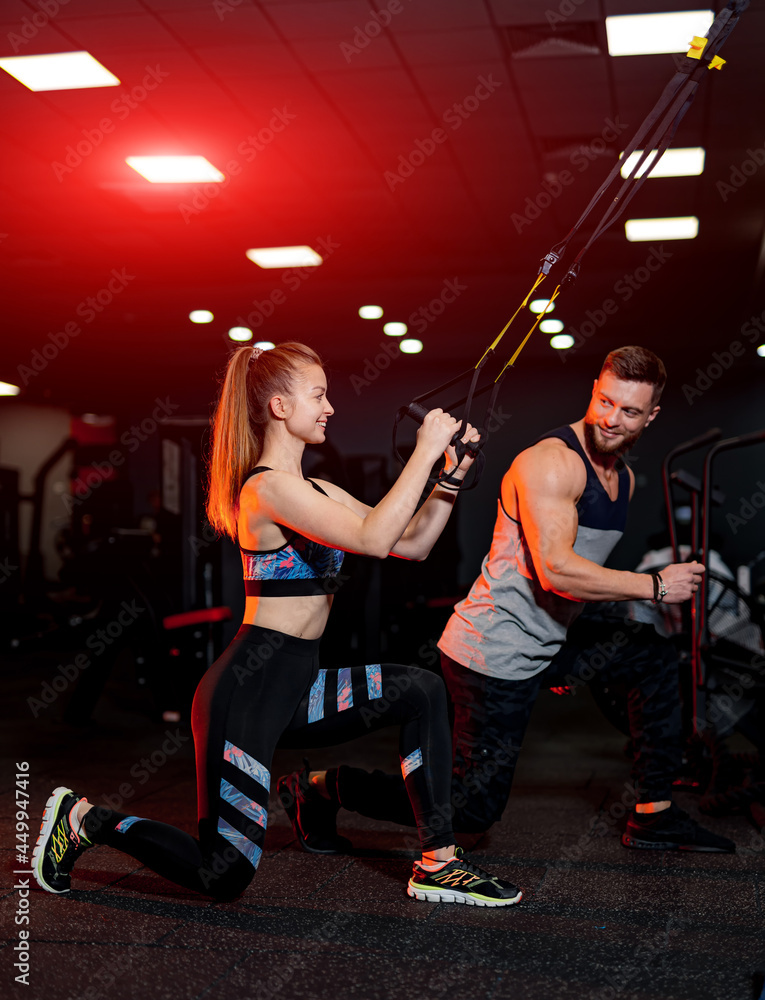 运动型情侣在健身房锻炼。年轻的运动型私人教练在帮助他的客户。