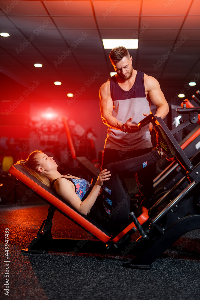 年轻的运动型私人教练在帮助他的客户。运动型情侣在健身房锻炼。