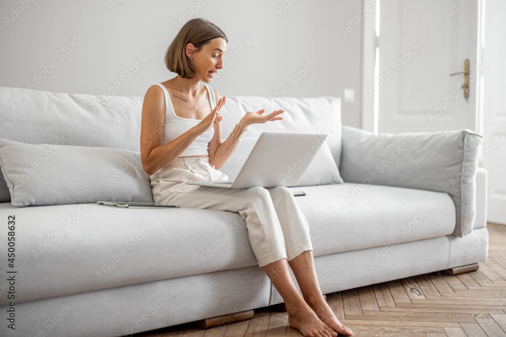 Young woman talking online on laptop, having a video conference while sitting on the comfortable cou