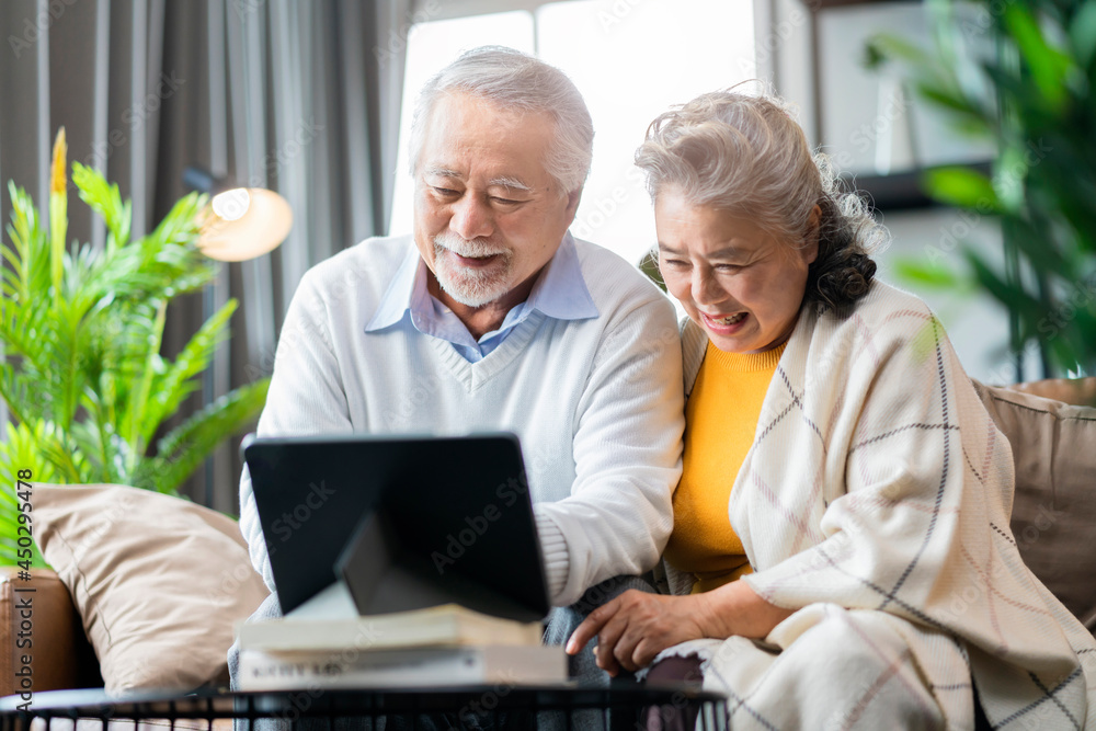一对亚洲老夫妇退休了，坐在沙发沙发上用平板电脑给家人视频通话