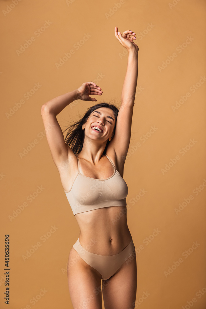 Portrait of young beautiful slim woman in lingerie posing isolated over brown studio background. Nat