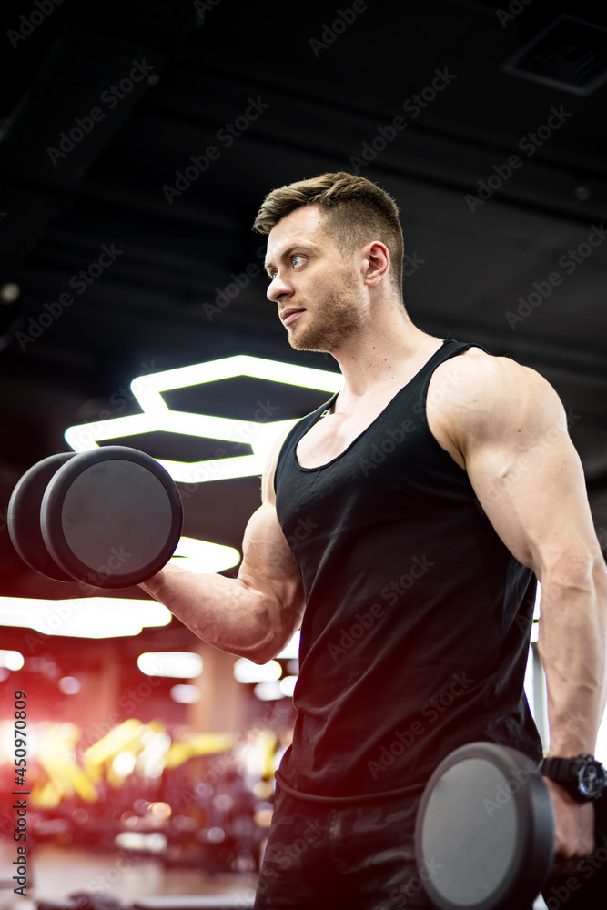 强壮英俊的男人在健身房努力工作。健美运动员训练他的二头肌。