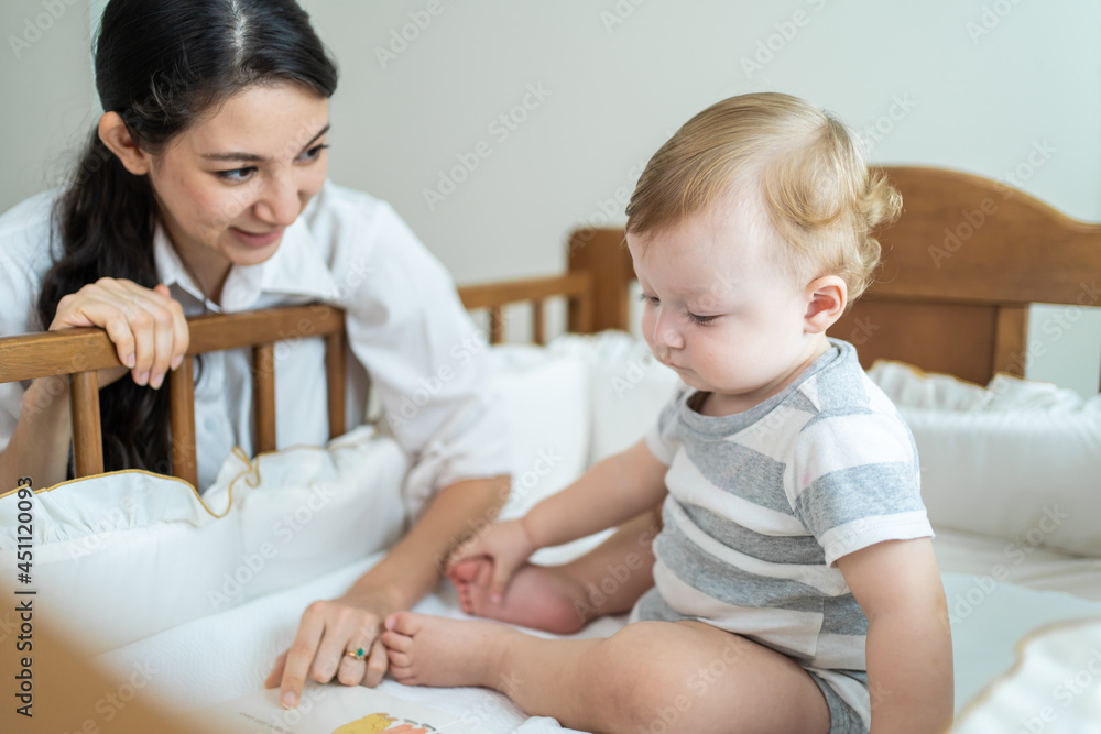高加索母亲在卧室的婴儿床上给婴儿读故事。
