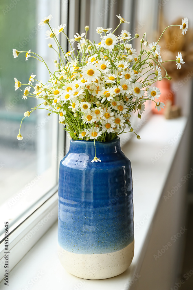 Vase with fresh chamomiles on windowsill