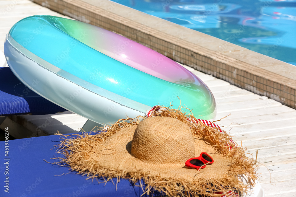 时尚的帽子、太阳镜和游泳池边缘的充气环