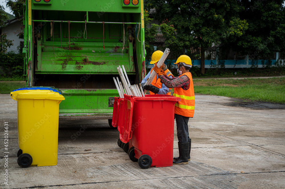 Garbage men working together on emptying dustbins for trash removal with truck loading waste and tra