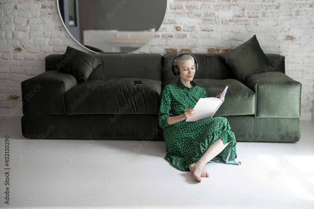 穿着绿色连衣裙的时尚女性坐在地板上看书听音乐nea