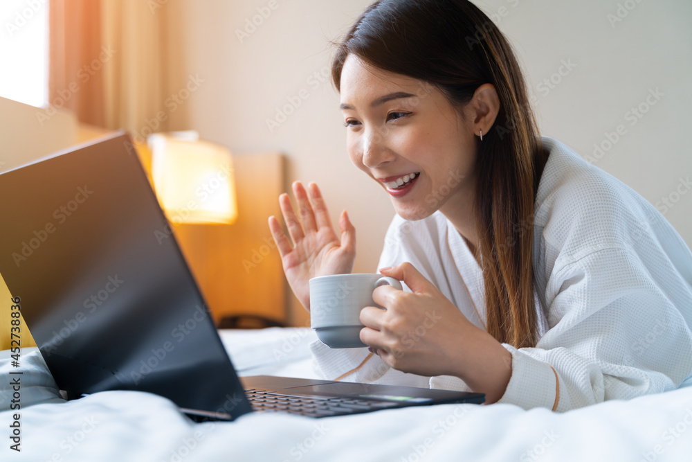 亚洲女性穿着浴袍，早上喝咖啡时用笔记本电脑进行视频通话的照片