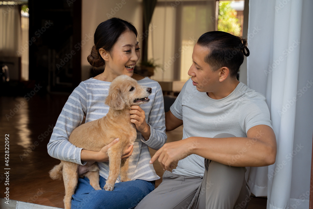 年轻的成年亚洲夫妇抱着一只小狗，背景是家里的内饰。30多岁的成熟女人抱着