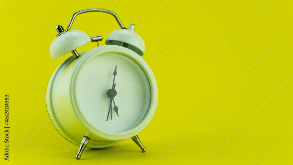 White alarm clock on yellow table background.