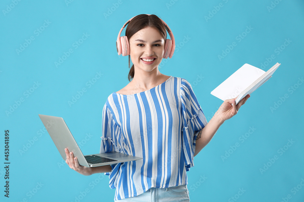 带笔记本电脑、书本和彩色背景耳机的年轻女性