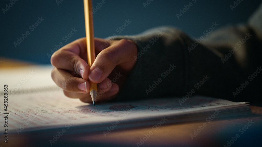 一个年轻人在笔记本上用铅笔写作的真实特写镜头。青少年在做作业