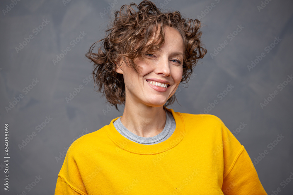 快乐快乐的年轻女人，留着短卷发，穿着亮黄色毛衣，化着自然的妆