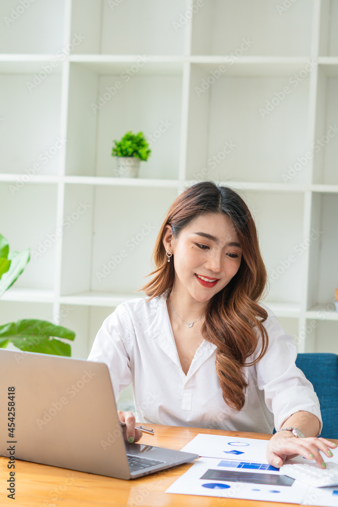 年轻的亚洲商务女性在办公室用笔记本电脑工作，桌上放着文件