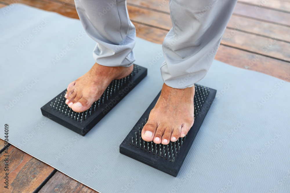 户外瑜伽课上，一名身穿灰色裤子的瑜伽男子赤脚站在带钉子的木板上
