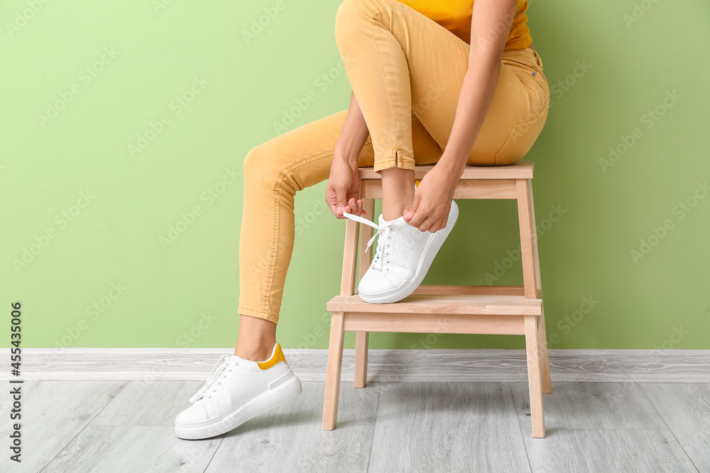 穿着时尚鞋子的女人坐在靠近彩色墙的凳子上