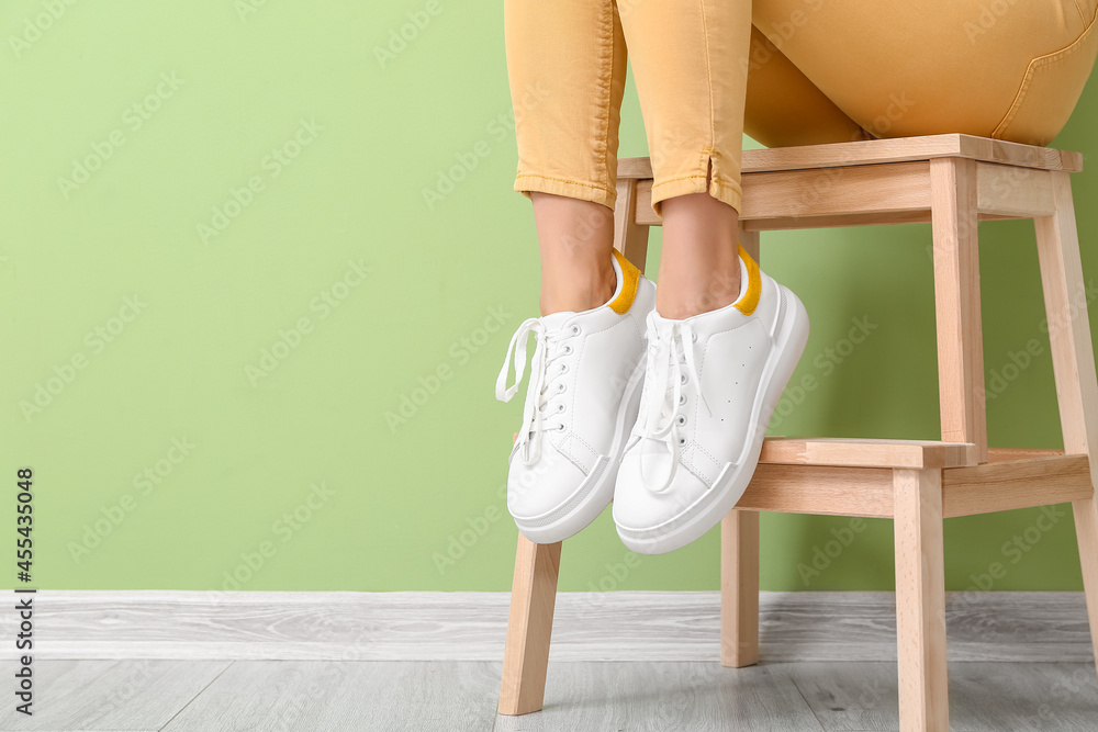 穿着时髦鞋子的女人坐在靠近彩色墙的凳子上