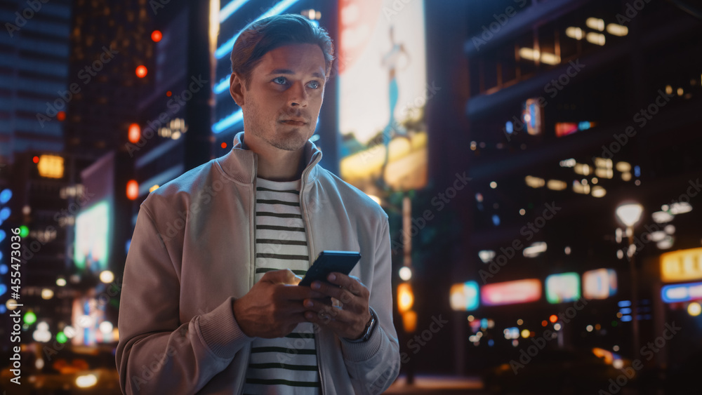 使用智能手机的男子在充满霓虹灯的夜城街道上行走的肖像。微笑的风格