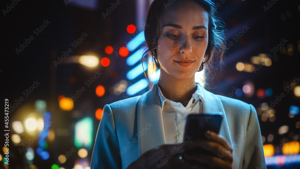 美丽的年轻女子使用智能手机站在充满霓虹灯的夜城街道上。波特拉伊