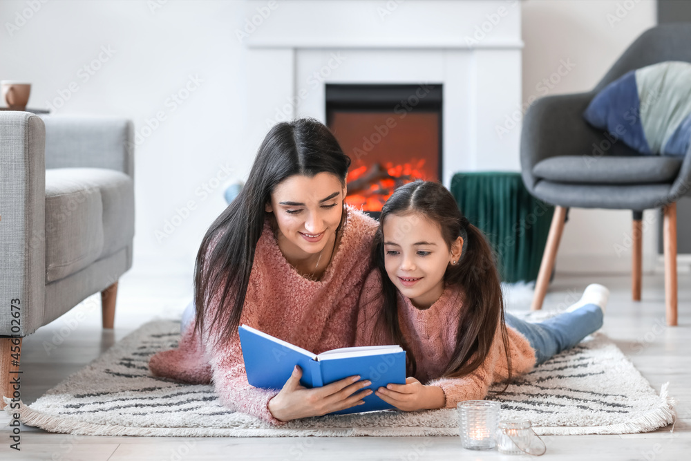 年轻的母亲带着女儿在家里的壁炉旁看书