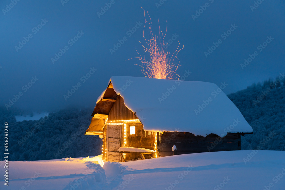 梦幻般的冬季景观，在白雪皑皑的森林中有发光的木屋。火苗从气中飞出