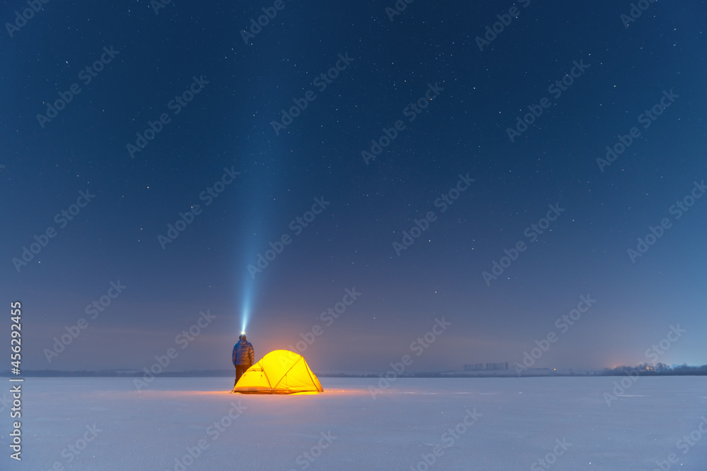 游客在黄色帐篷附近拿着手电筒，在不可思议的背景下从里面照亮