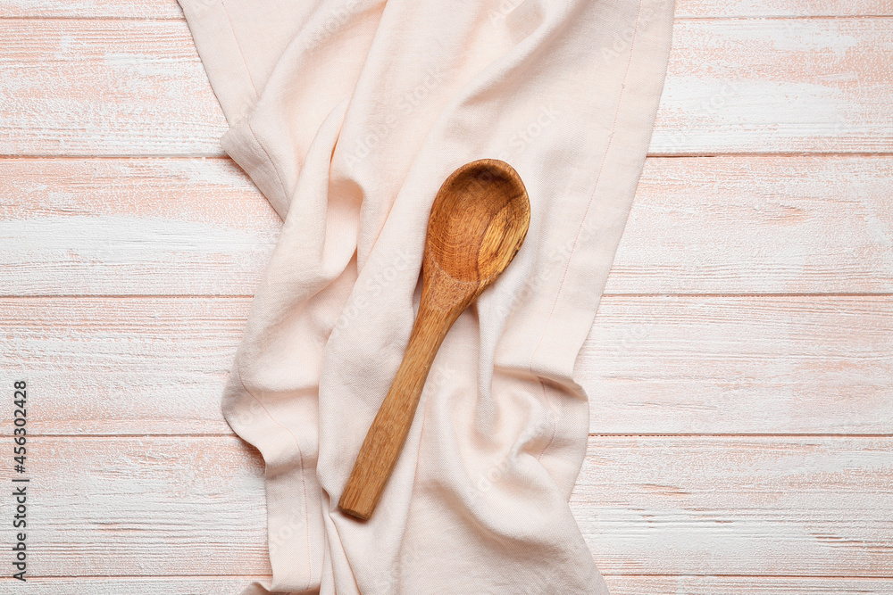 浅色木质背景上的织物餐巾和勺子
