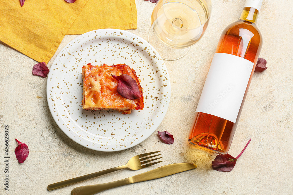 美味的千层面，盘子里有番茄酱，餐具和一瓶葡萄酒放在浅色桌子上