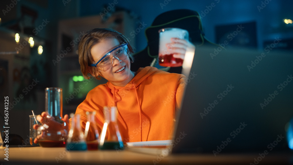 戴着安全护目镜的聪明男孩在家里用烧杯混合五颜六色的化学物质。青少年进行E
