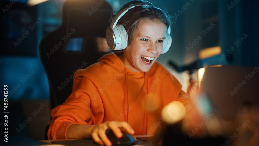 兴奋的年轻男孩戴着耳机在家里舒适的暗室里用笔记本电脑玩电子游戏。哈