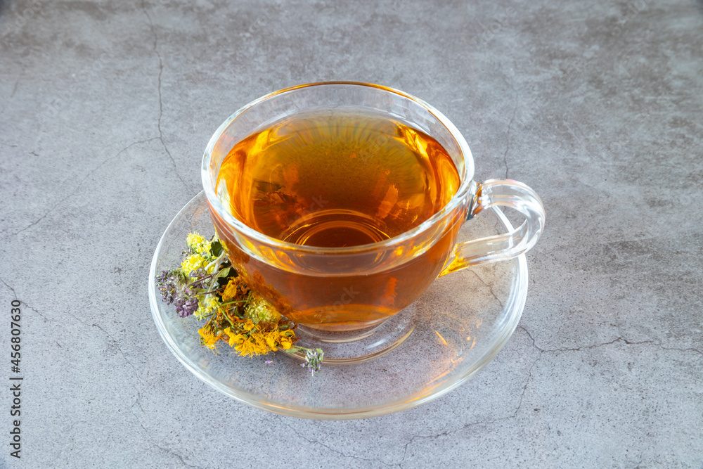 Cup of herbal tea with natural dried herbs on gray background.