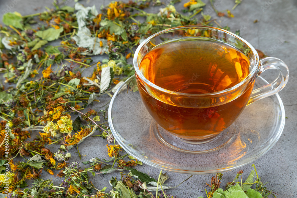 Cup of herbal tea with natural dried herbs on gray background.