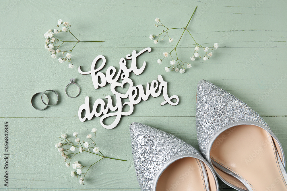 新娘鞋、结婚戒指和订婚戒指，在绿色木背景上写下有史以来最美好的一天