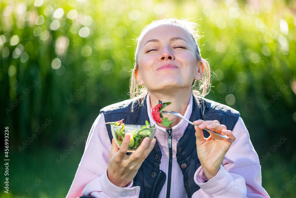 美丽的高加索女人在绿色自然背景下吃沙拉