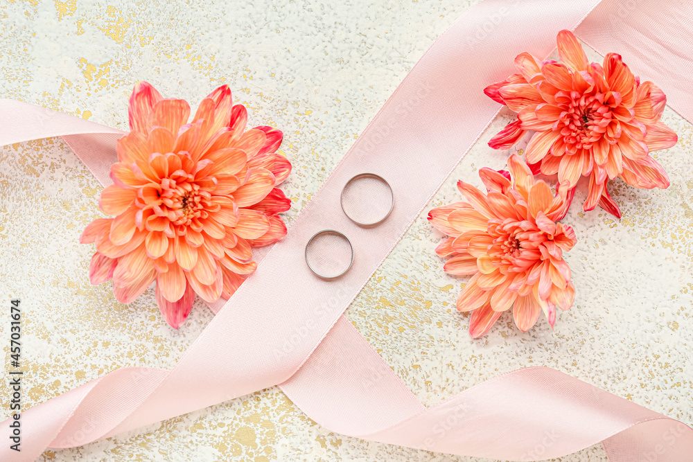 一对结婚戒指、缎带和彩色背景上的美丽花朵