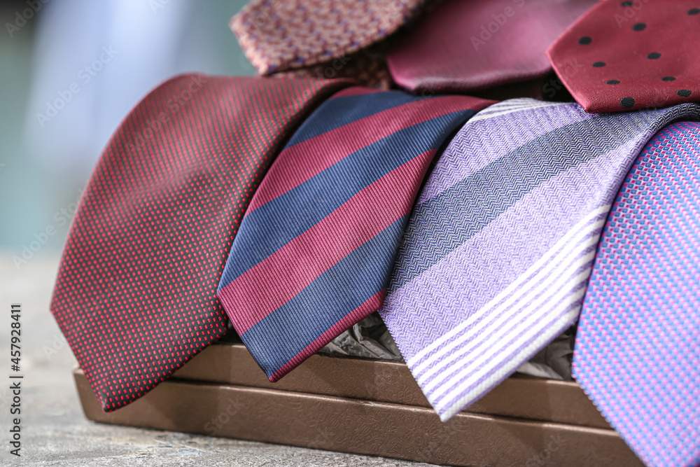 Box with many stylish neckties on table, closeup