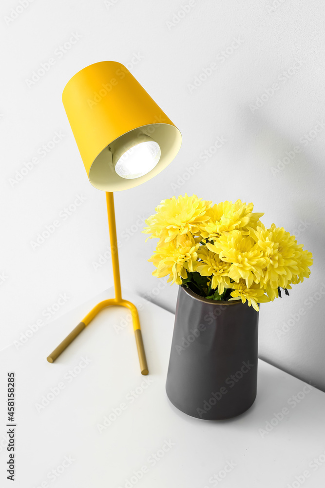 白色墙壁附近的桌子上放着一个花瓶，花瓶里有美丽的花朵和发光的灯