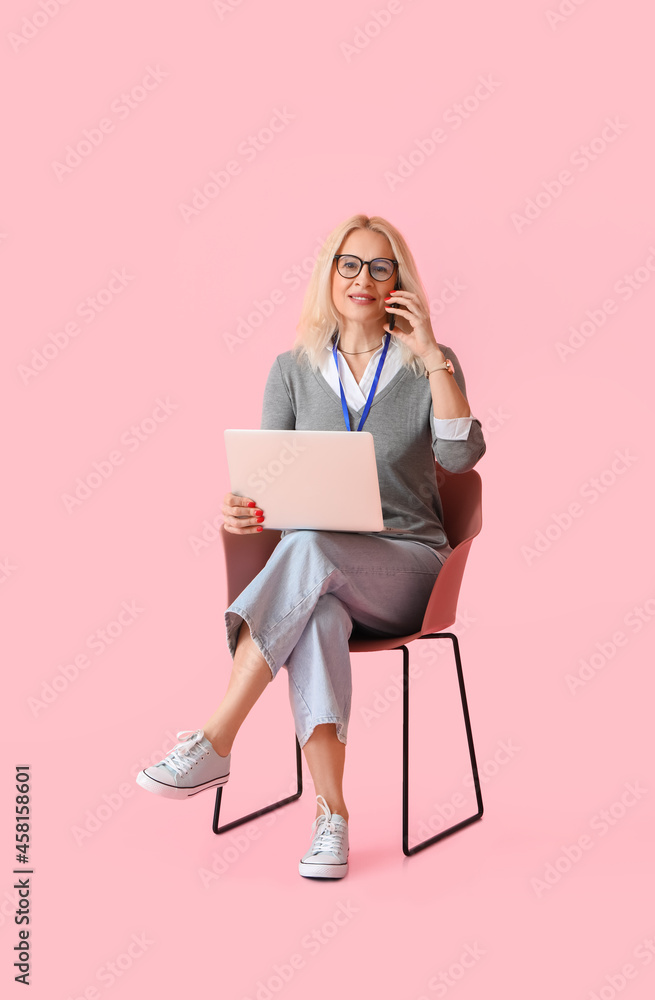 一位拿着笔记本电脑的成熟女商人坐在椅子上对着b色打电话的肖像