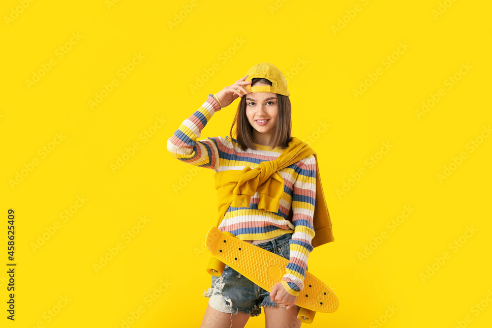 Beautiful female teenager with skateboard on yellow background